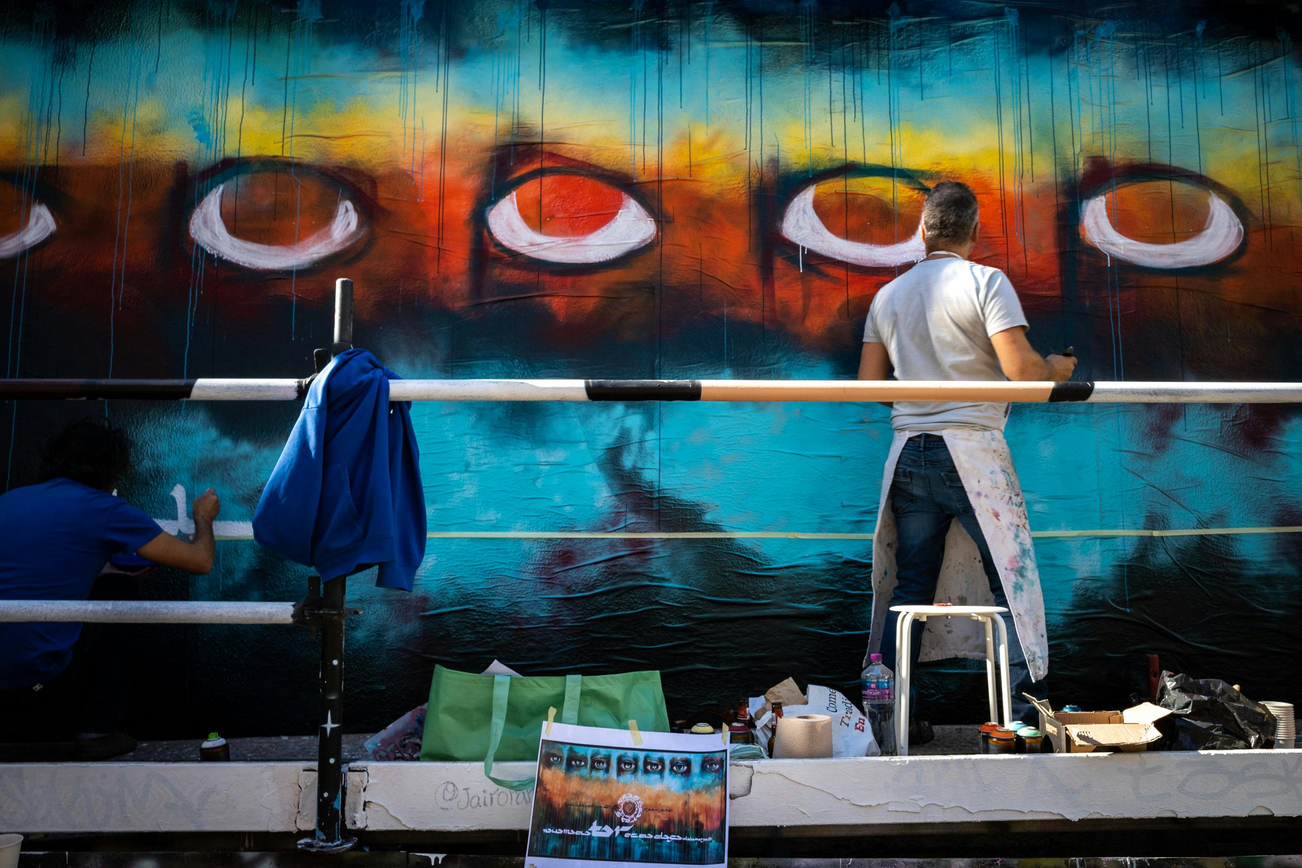 A man painting a mural with 5 eyes