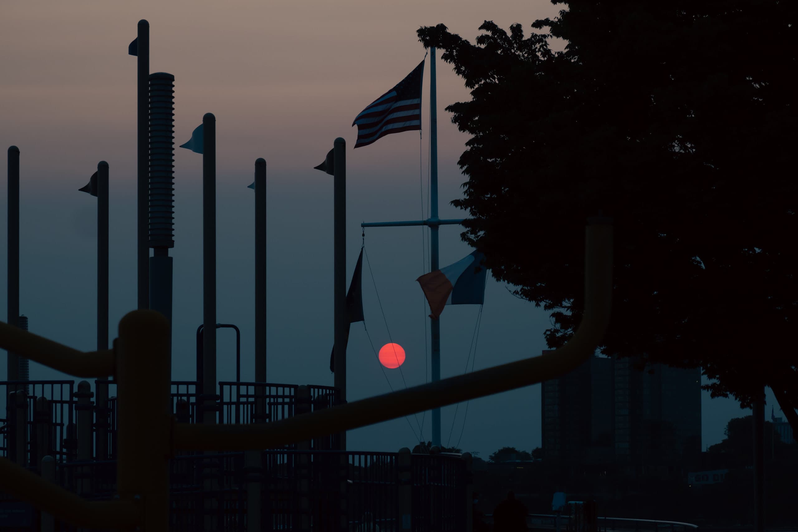 A red sun behind a playground with an American flag on a pole