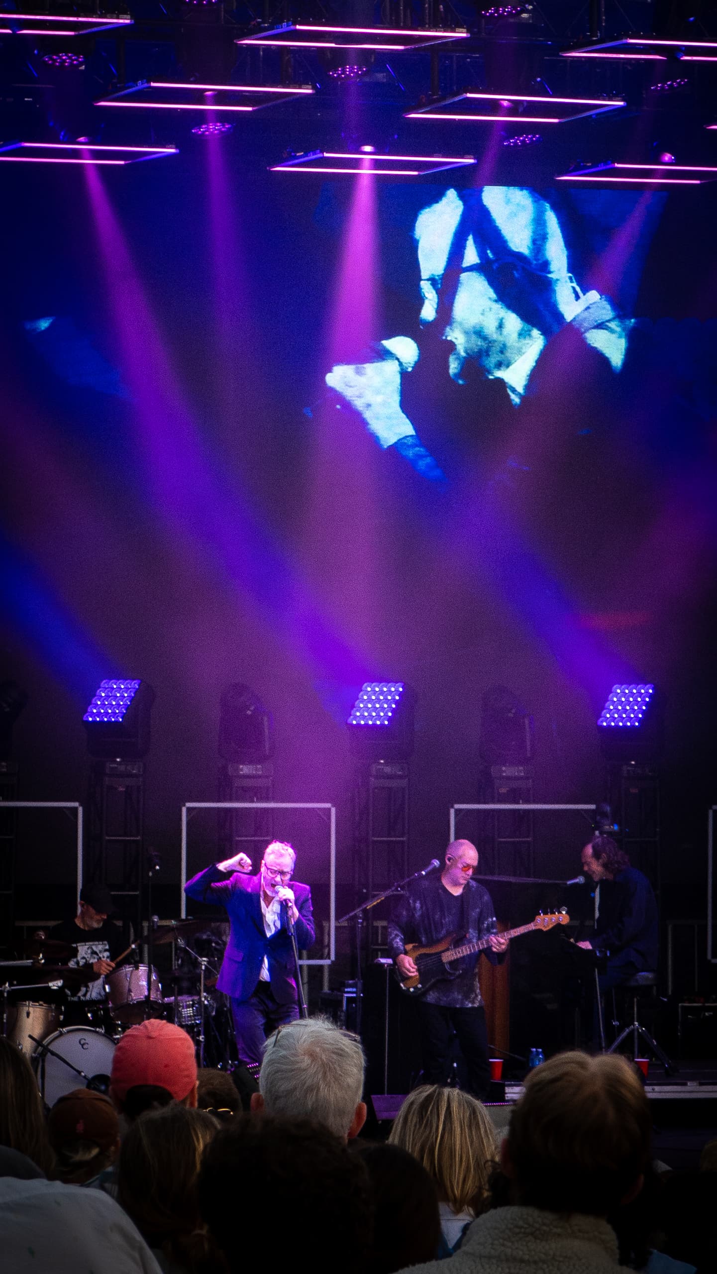 Male singer with directional purple lights on him on stage in a concert with people in front