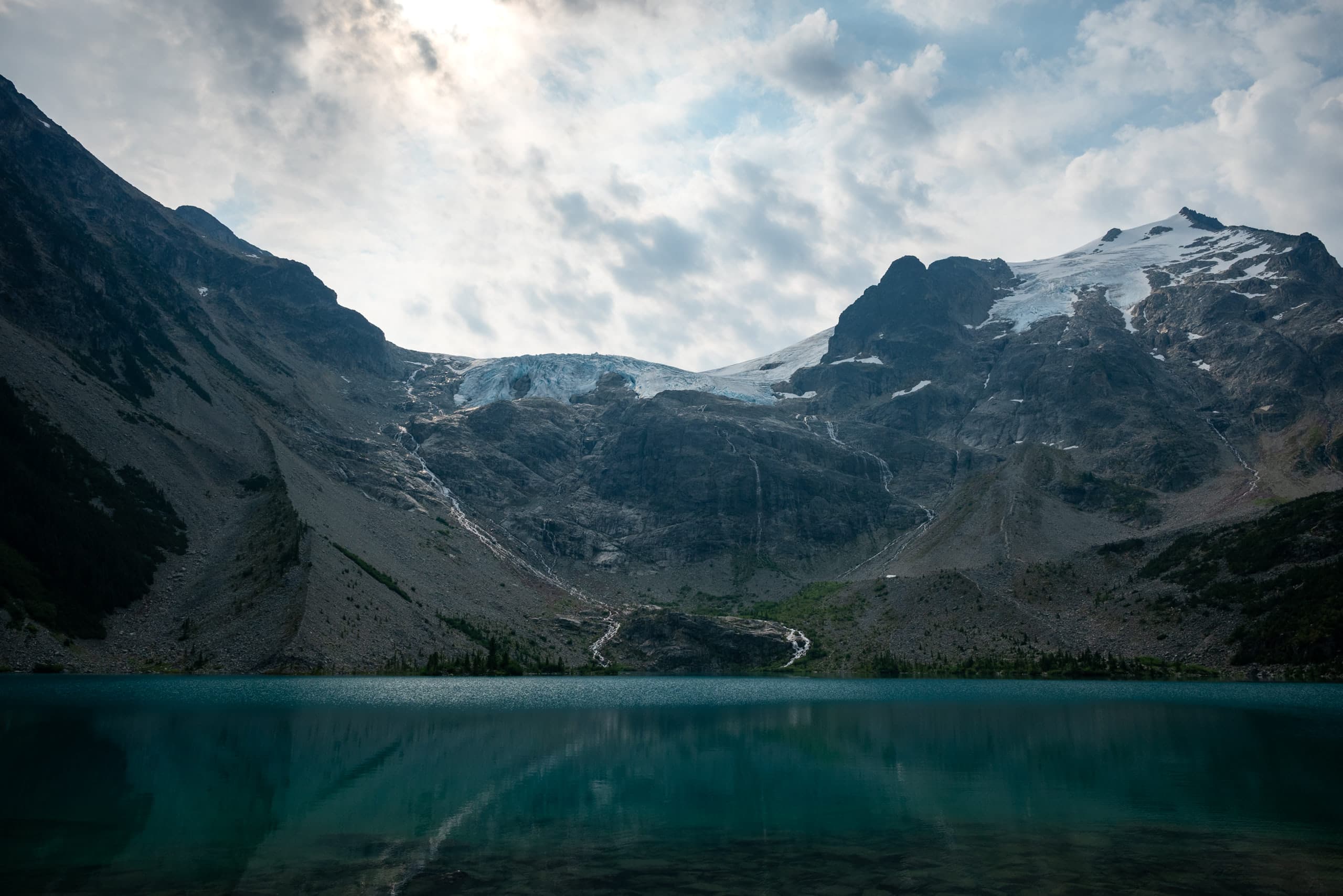 Landscape photo of a moutain with glacier at the top and a stream of water going into a turquoise lake in the foreground