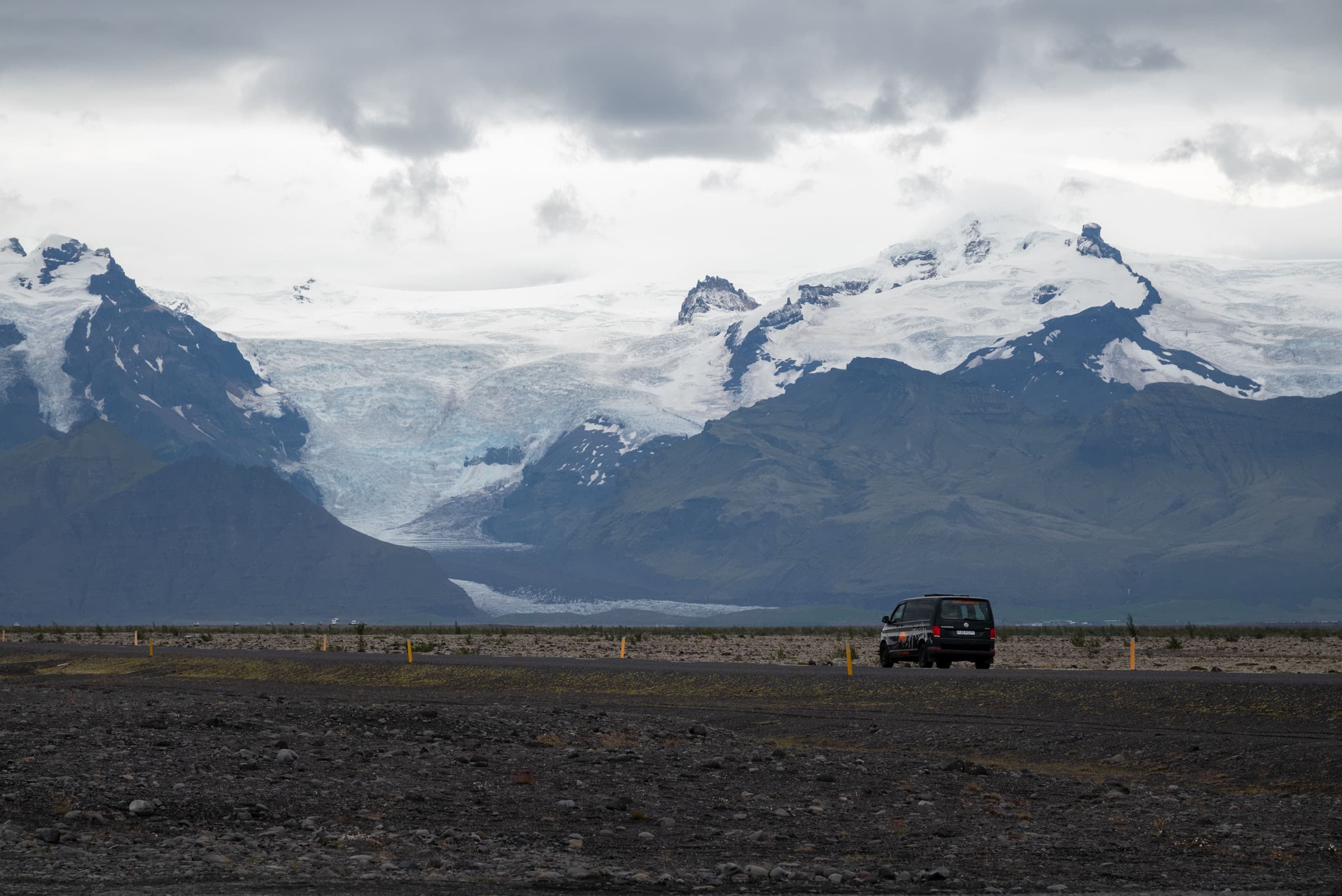 A car driving from left to right into the mountains and a glacier in the distance