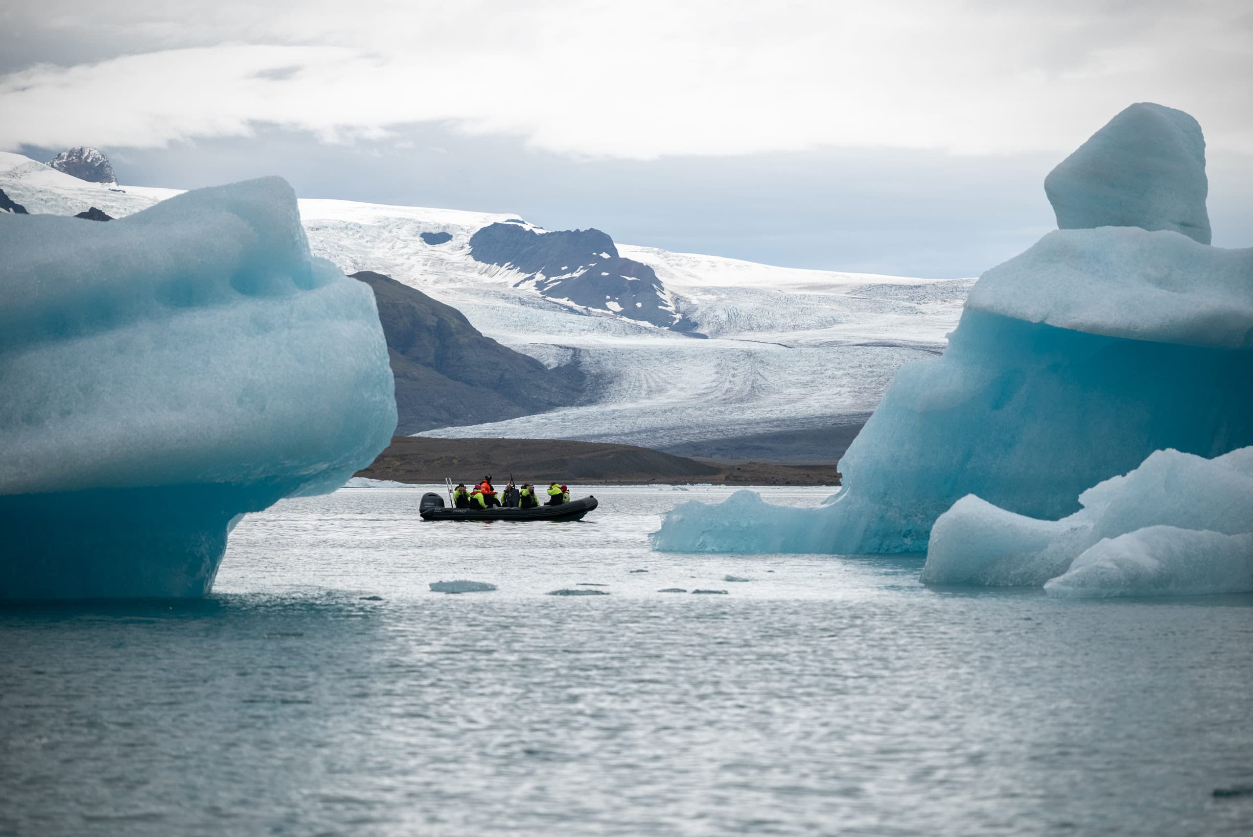 A small boat with tourists cruising between two large icebergs with a large glacier in the background