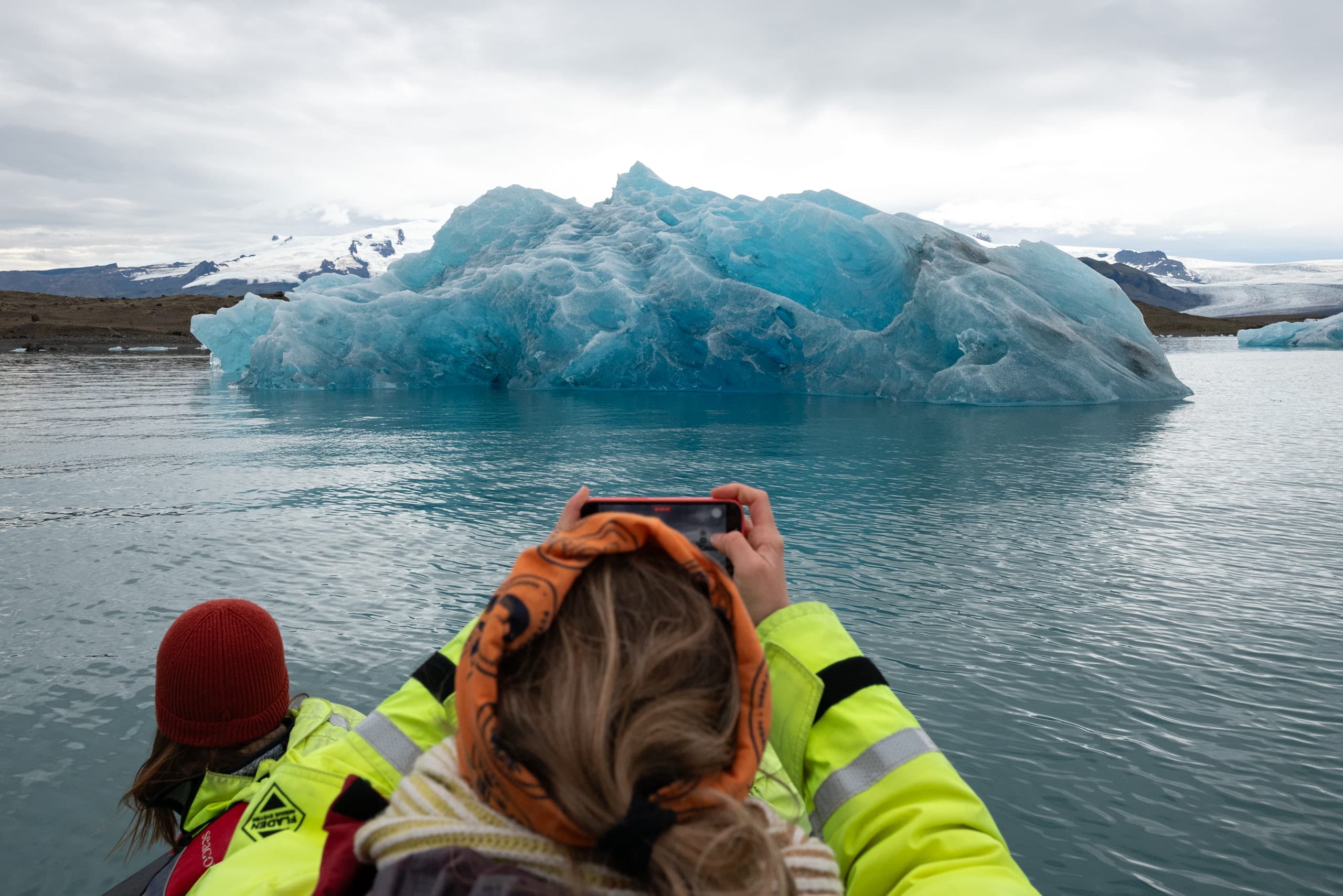 A woman taking a photo of a large upside down iceberg with her phone