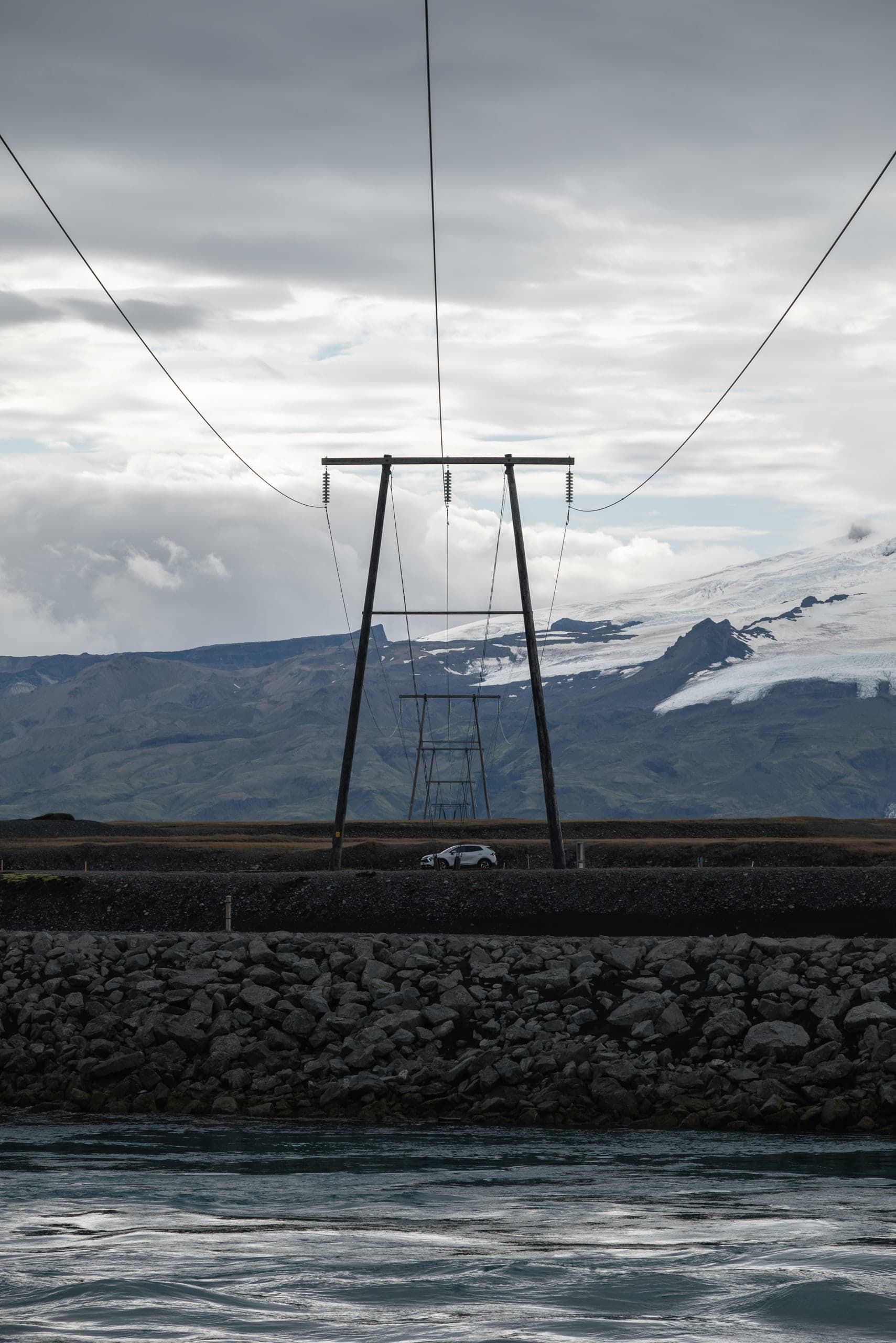 A car in the center driving across a road and power lines cascade into the distance at the center