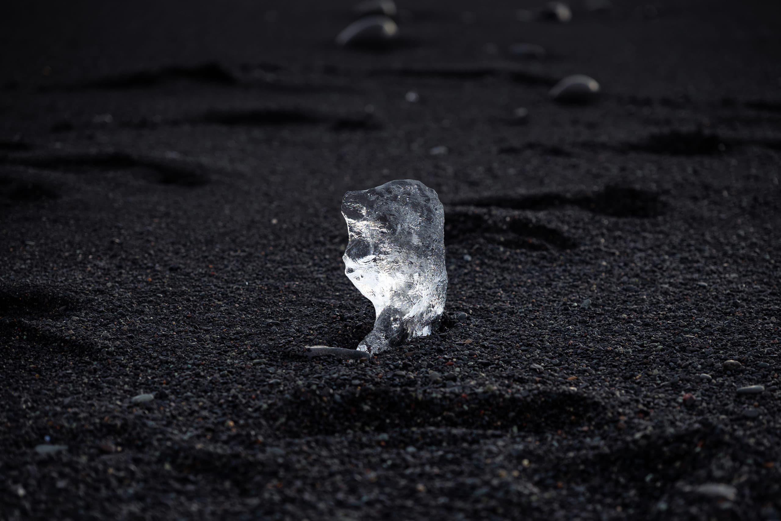 A close up of a piece of transparent ice on black sand