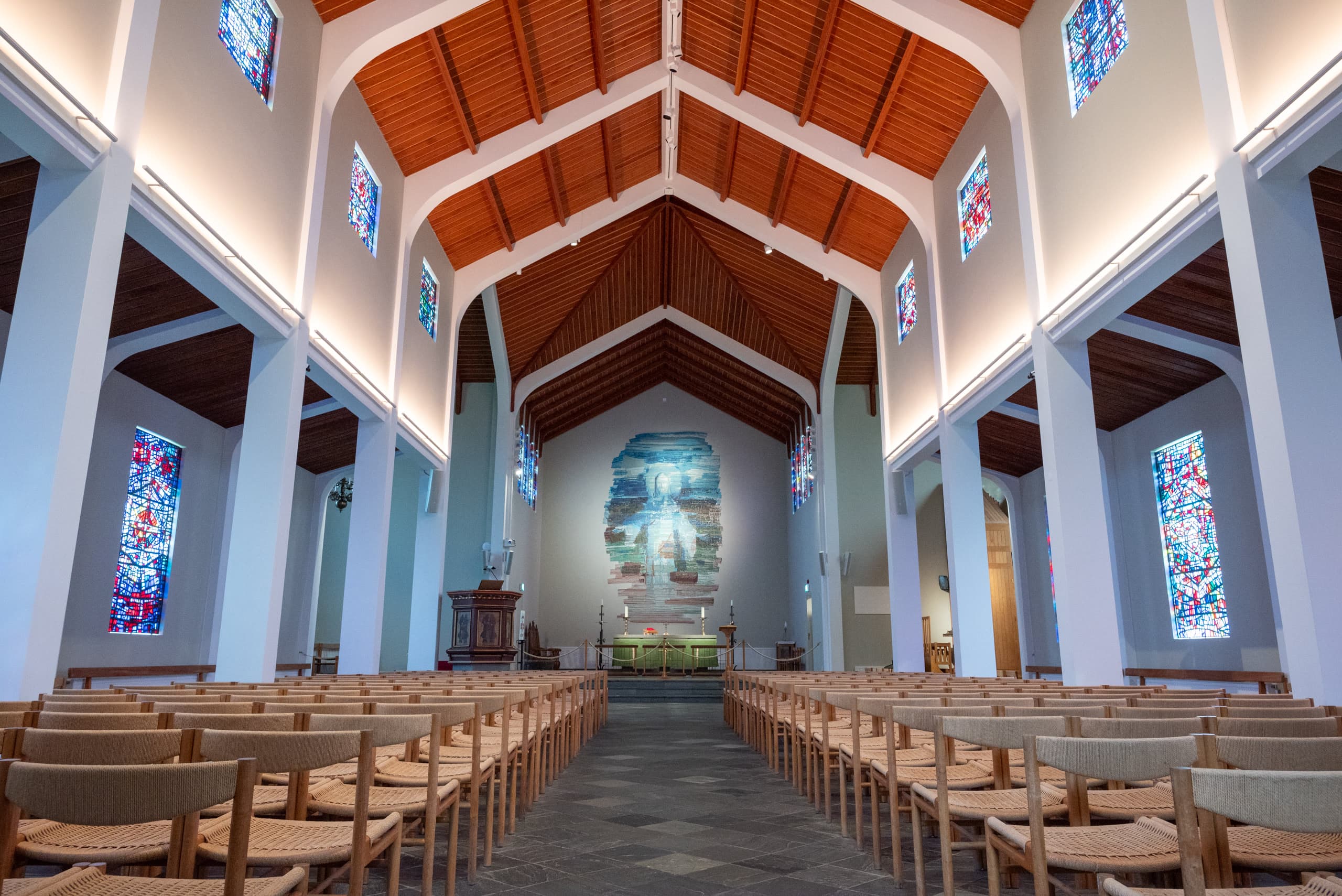 Inside an Icelandic church with rows of wooden chairs facing a mural of Jesus