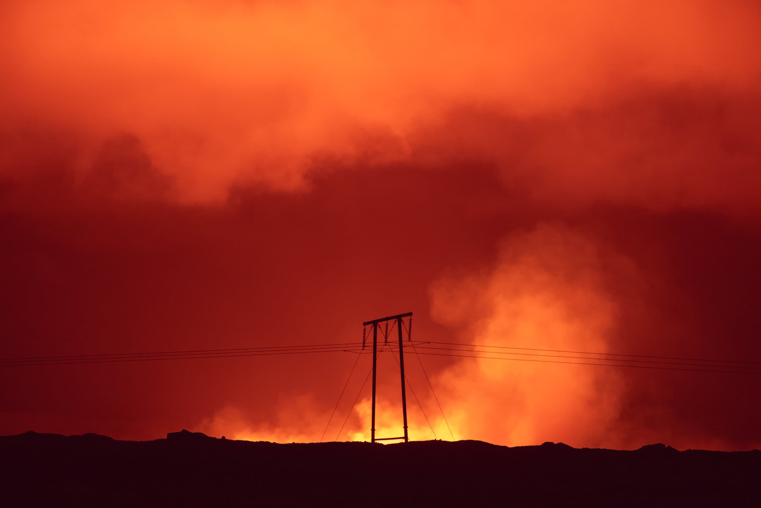 A silhouette of a power line with a bright orange sky in the background at night