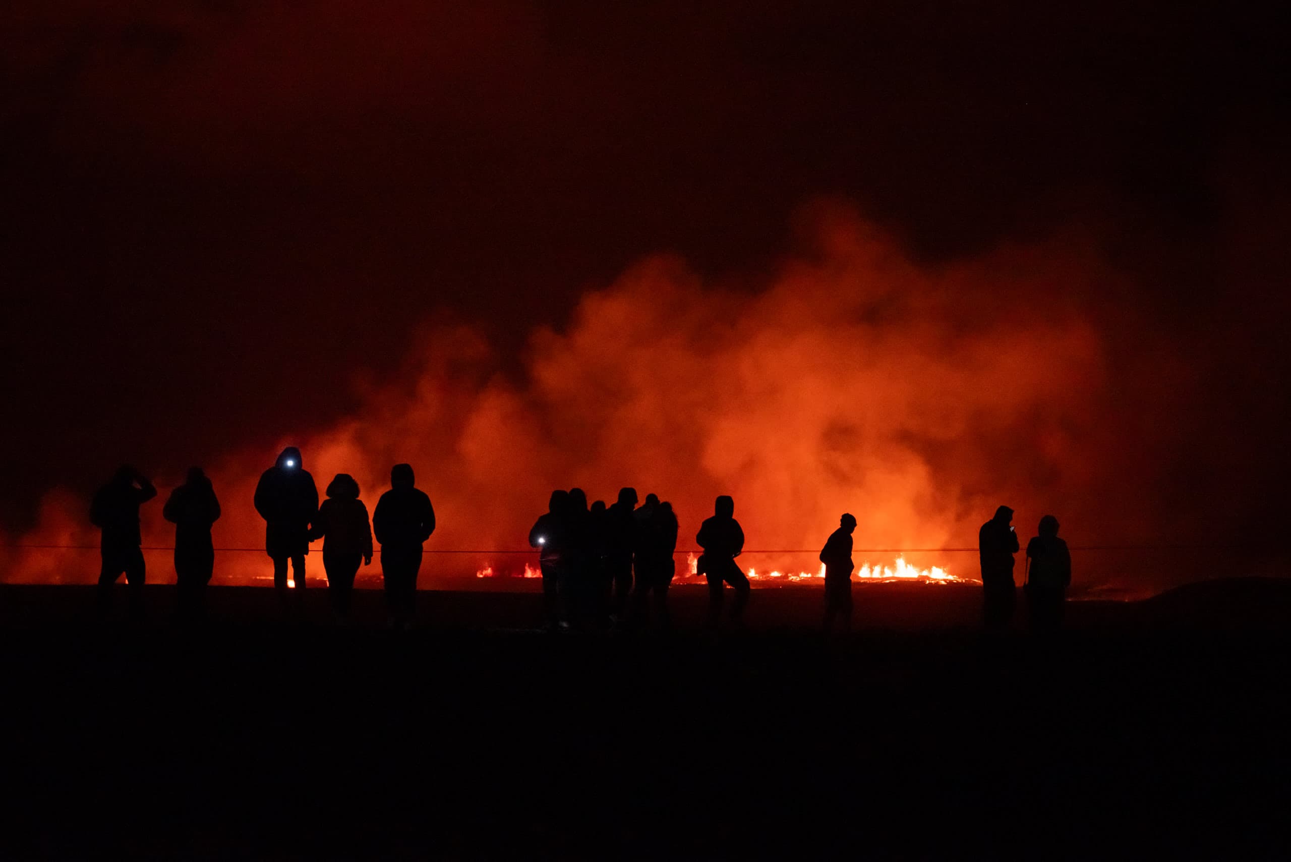 Silhouette of people against the backdrop of an active volcanic fissure with brightly lit smoke at night