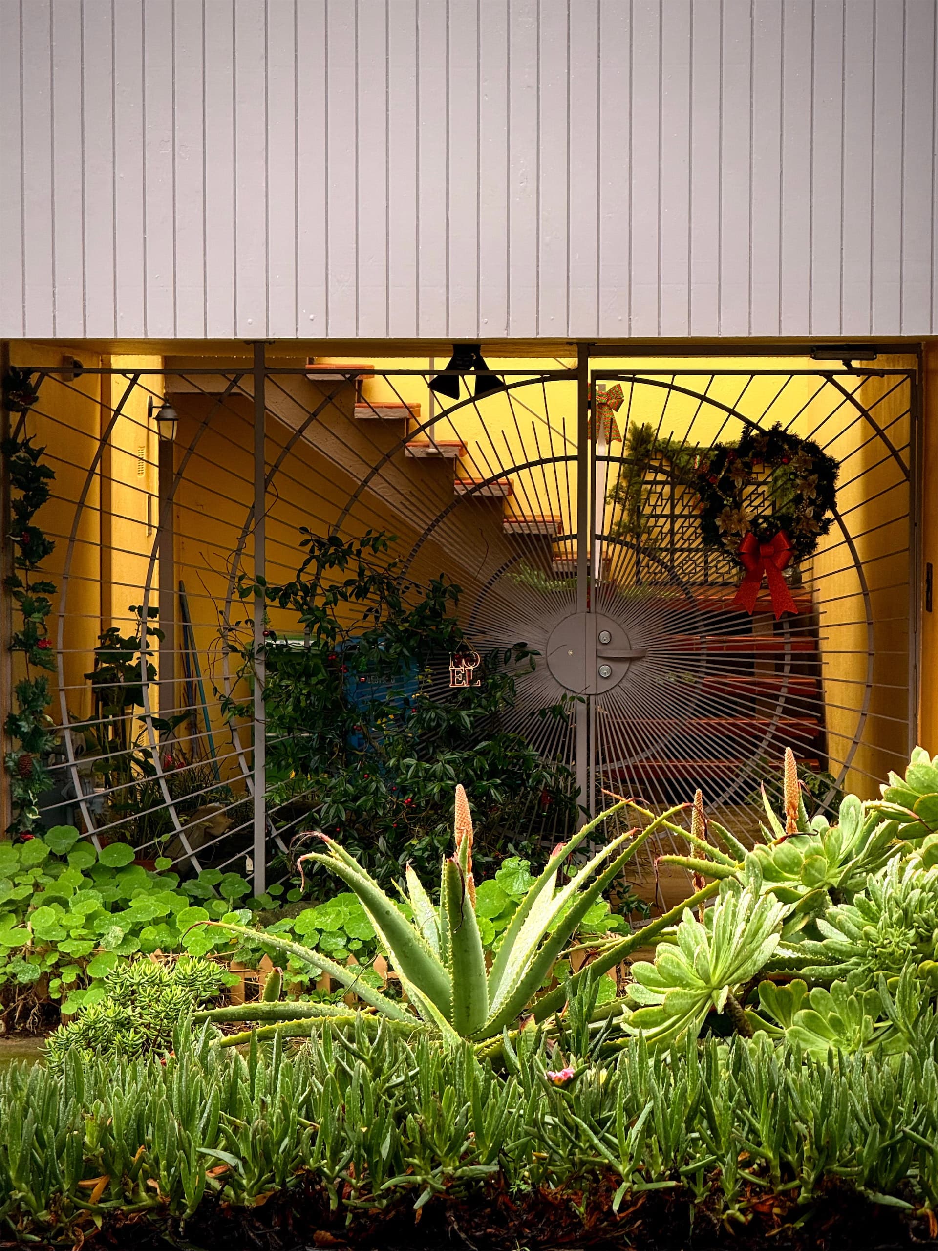 A yellow entrance with a large radial gate and plants in the foreground